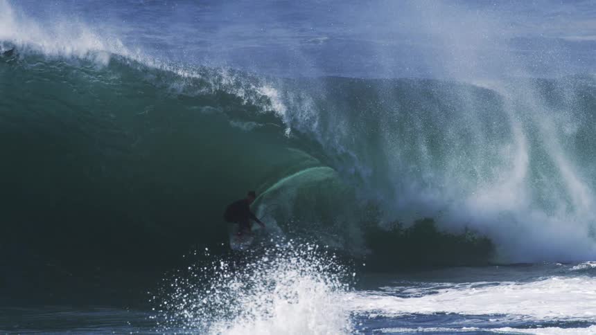A surfer braves a massive barreling wave with spray and foam exploding around them