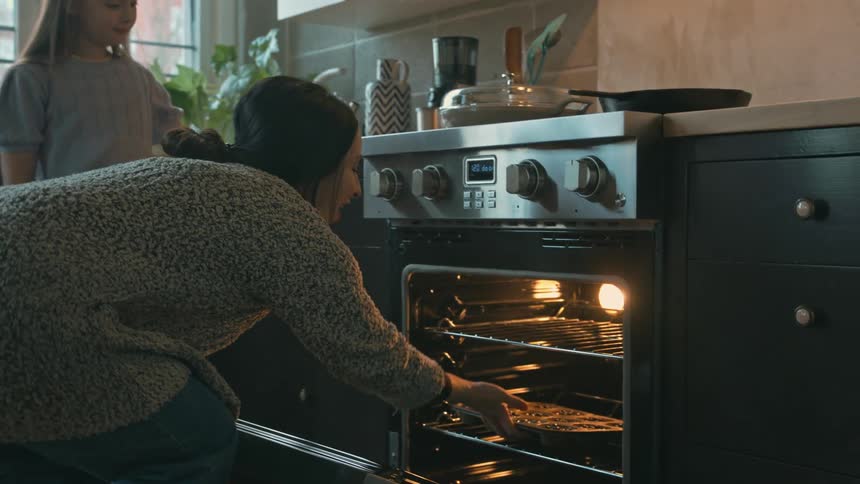 A mother and daughter put muffins in the oven to cook