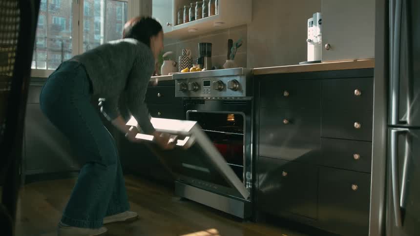 A woman is in a kitchen opening an oven and placing a casserole dish inside