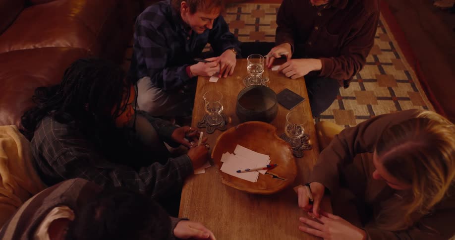Friends sitting around a table writing on small white papers