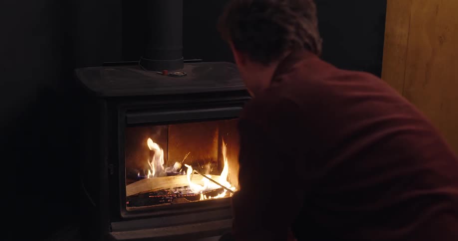 A man adding wood to the stove inside his home and closing the stove door