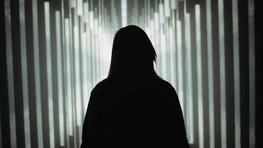 A person is standing in a corridor surrounded by strobing light and shadow