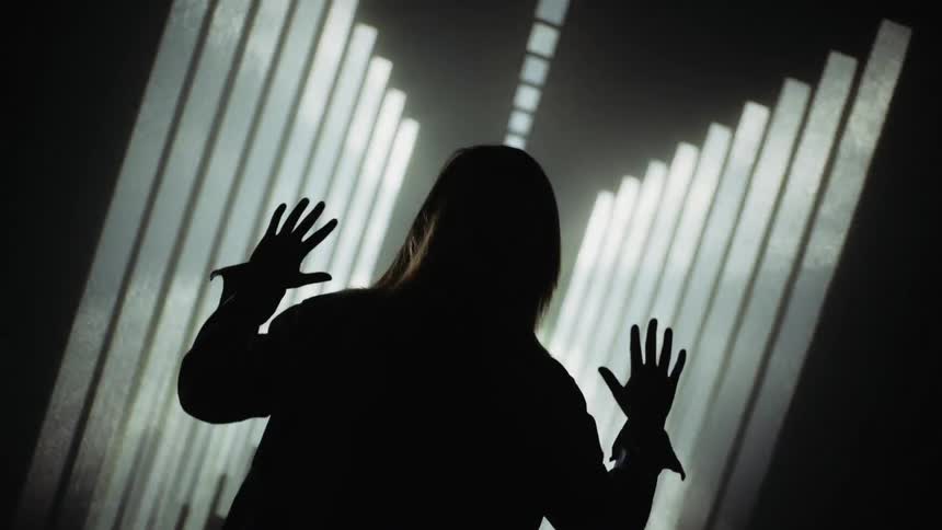 A person is raising their hands as they stand in a front of a projection of lights