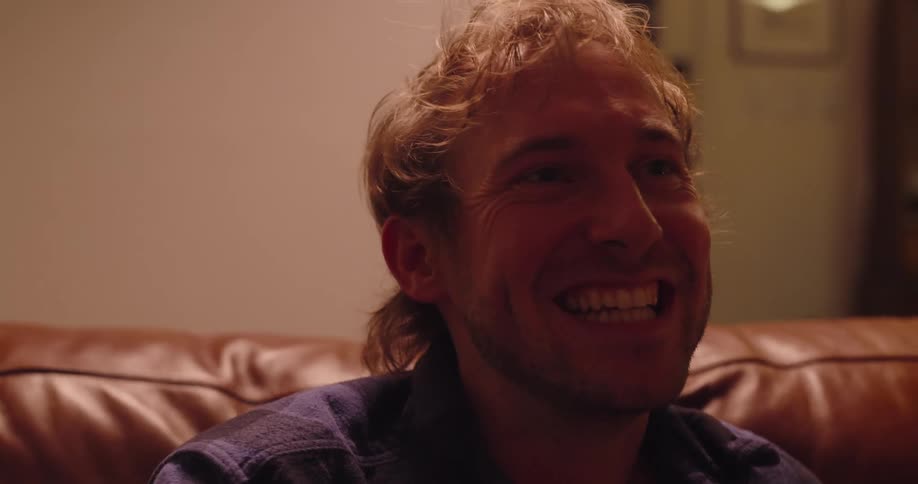 Man laughs as he sits on the couch and talks to someone