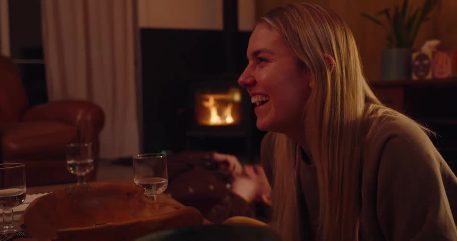 A group of people are laughing and enjoying a meal together in a warmly lit room with a fireplace