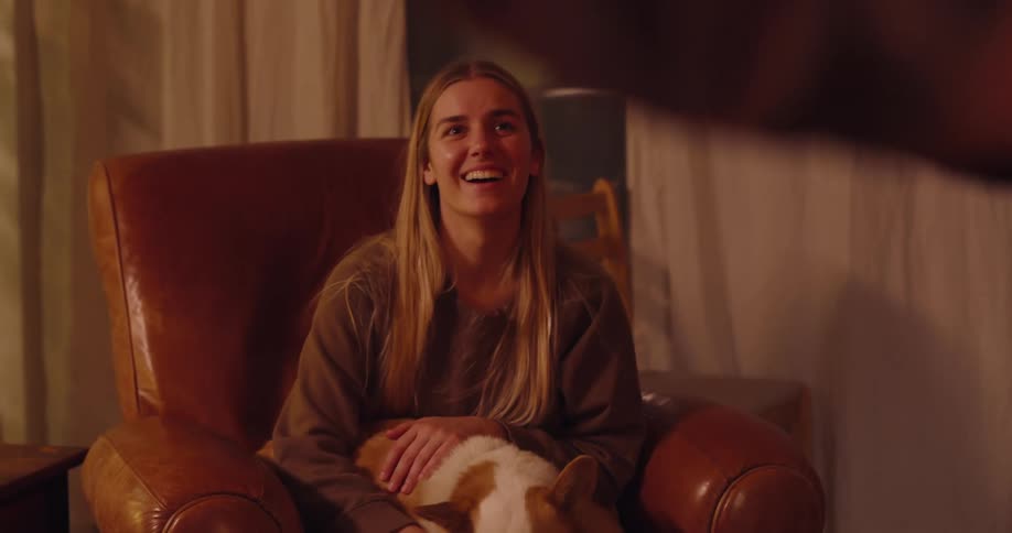 Woman sitting in an armchair with a laughing dog and watching another person standing there moving their hands