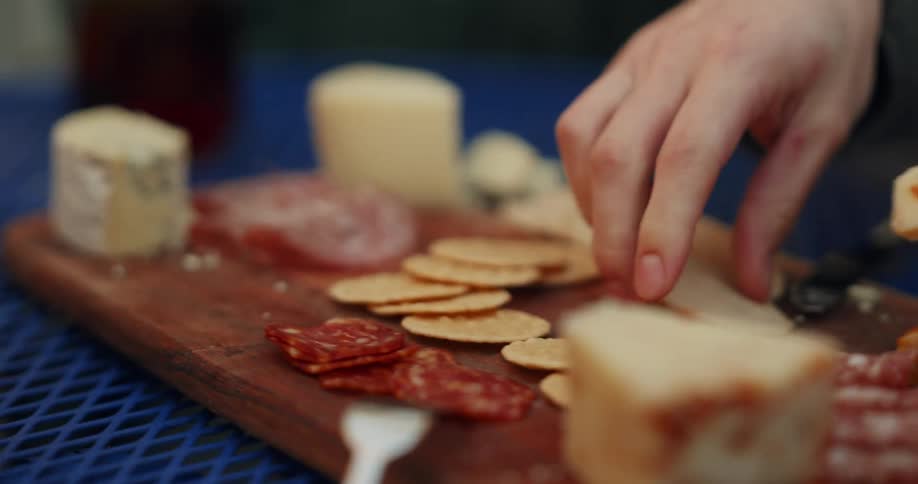 Cutting a slice of cheese picking up crackers and salami from a chartreuse board