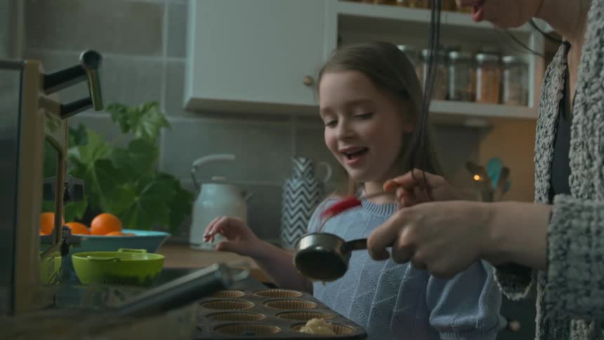 Mother and daughter cooking together by pouring batter into molds