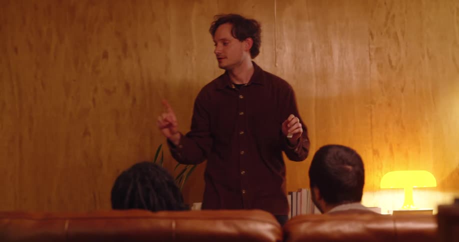 In a cozy dimly lit living room a group of friends animatedly play charades