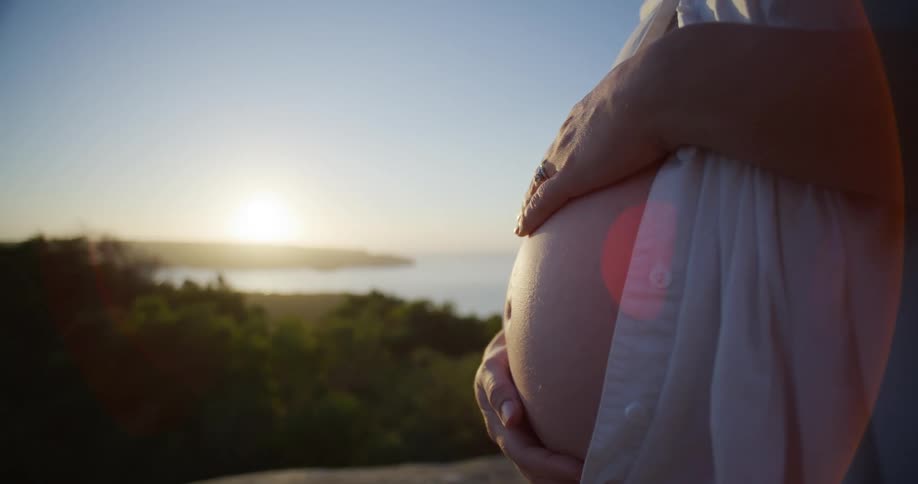 A man is caressing his pregnant wifes womb while theyre watching the sunrise over a lake