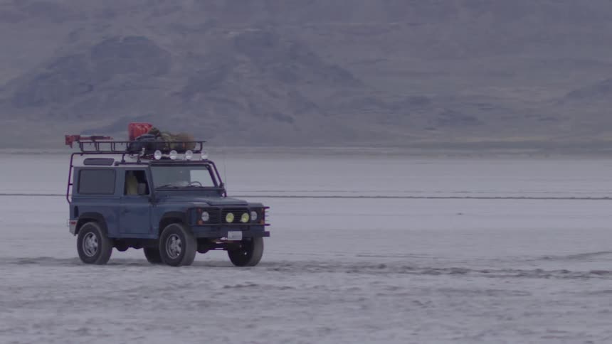 A vehicle drives in a flat sandy area
