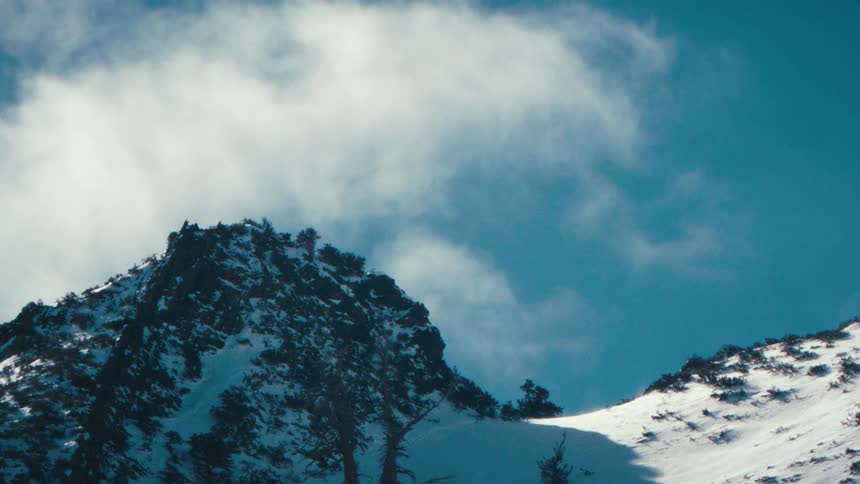 Clouds move in the sky above a snow covered mountain