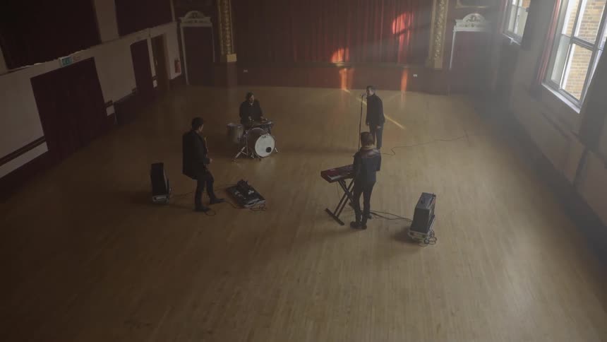 A fourmember band performs in an empty hall lit by natural window light