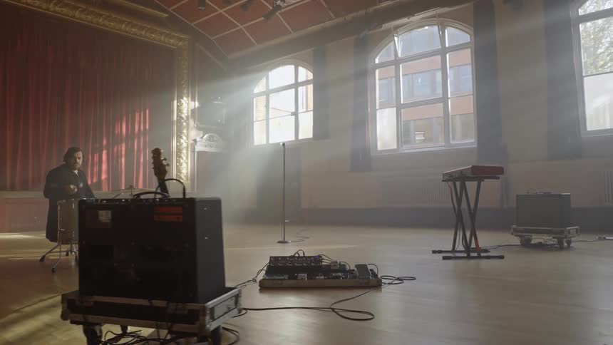 A man inside an empty hall filled with musical instruments plays a drum at midday