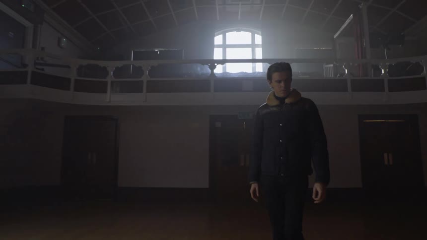 A man walks into a large room and goes to a piano keyboard