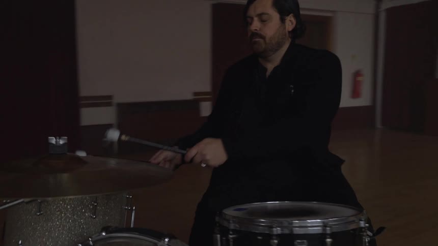 A drummer drums and rehearses with a band in a large room