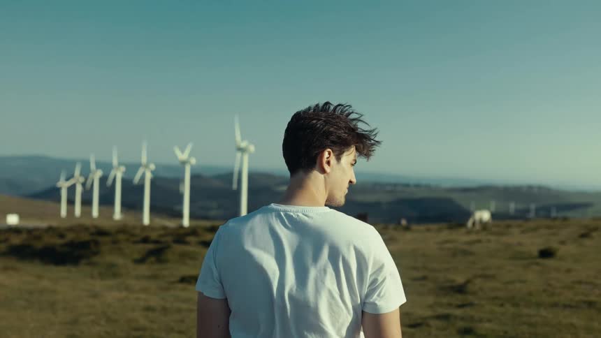 Back of man standing on a wind farm as the wind blows across his shirt