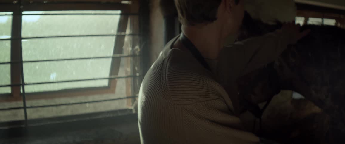 Man in a stable interacting with a brown horse next to him