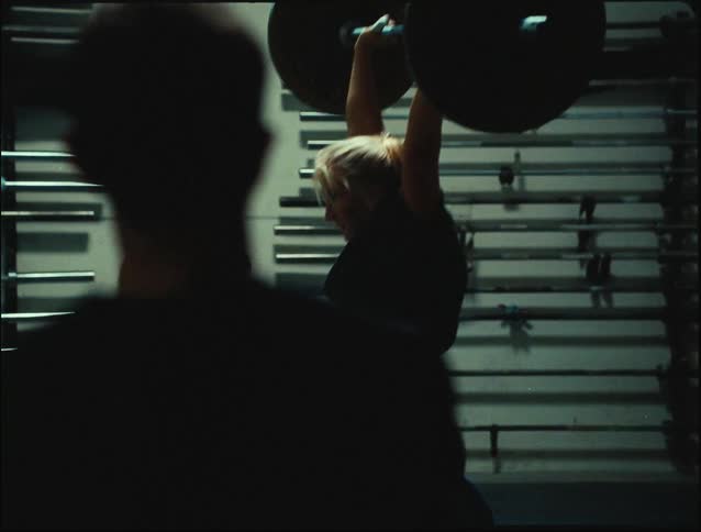 Man watches a woman lift a heavy weight bar in a gym