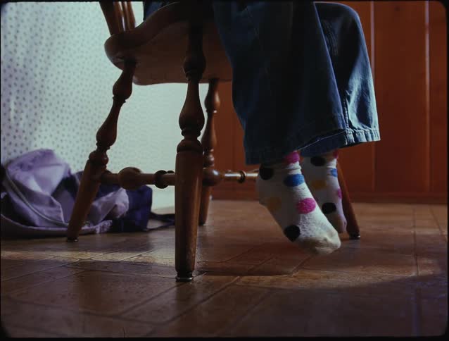 A child sits on a wooden chair with their socked feet playfully dangling above the floor