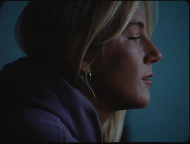 A woman sits quietly in profile gazing thoughtfully out of frame in soft moody lighting