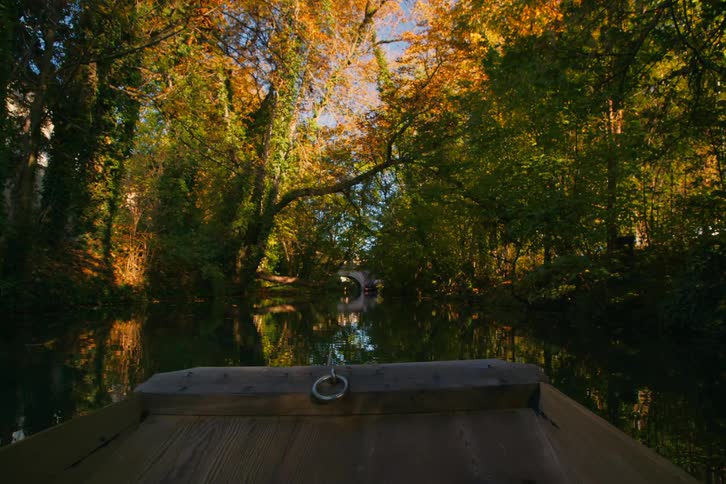 A wooden boat travels down a creek on a sunny autumn day