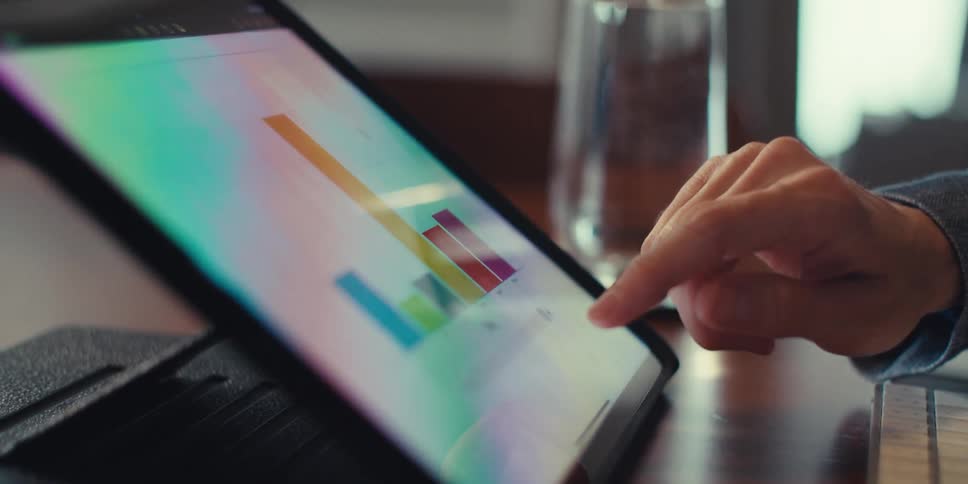 A person is interacting with a tablet displaying colorful bar graphs suggesting data analysis or a business presentation in a professional setting