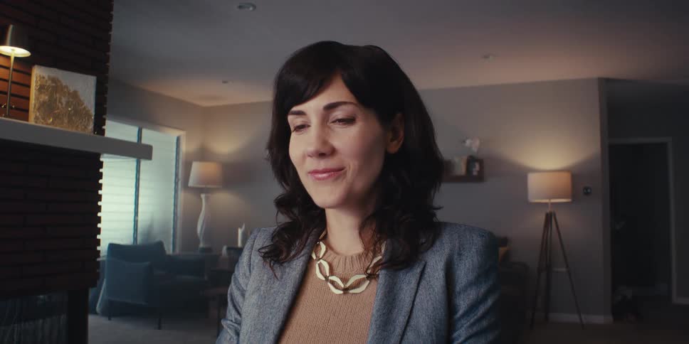 A woman wearing a suit and a gold necklace types on a keyboard in front of her computer smiling with a sigh of relief after completing the process
