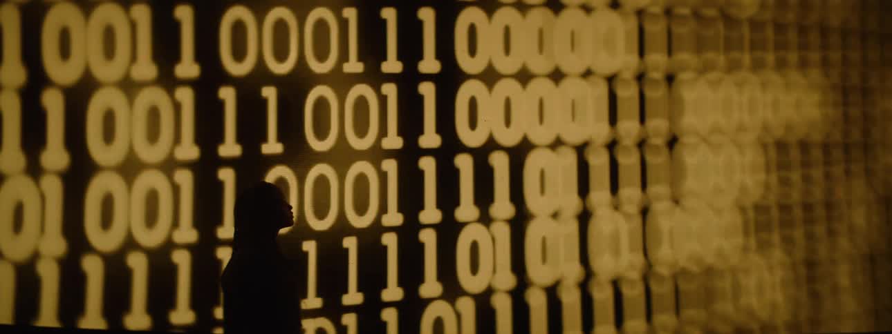 A woman standing in front of a large screen showing binary code on it