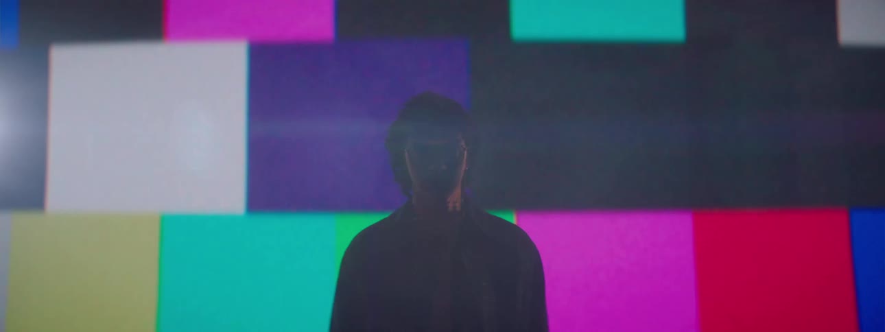 A man stands still with a neutral expression as glitchy colorful lines flash behind him