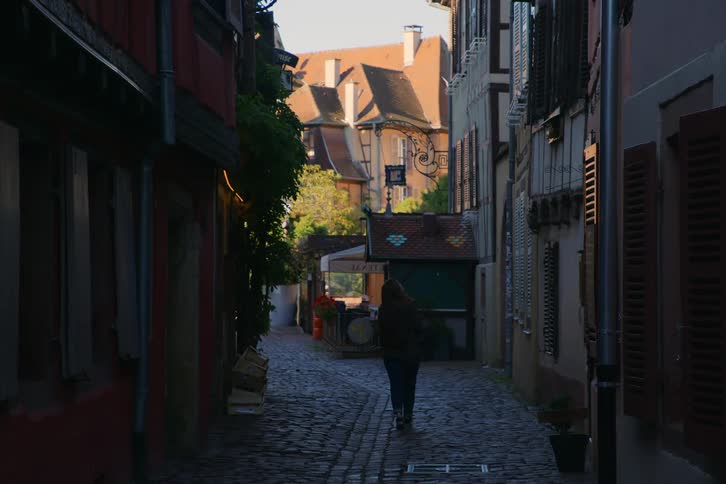 Person walks down a narrow shaded street in a historic city