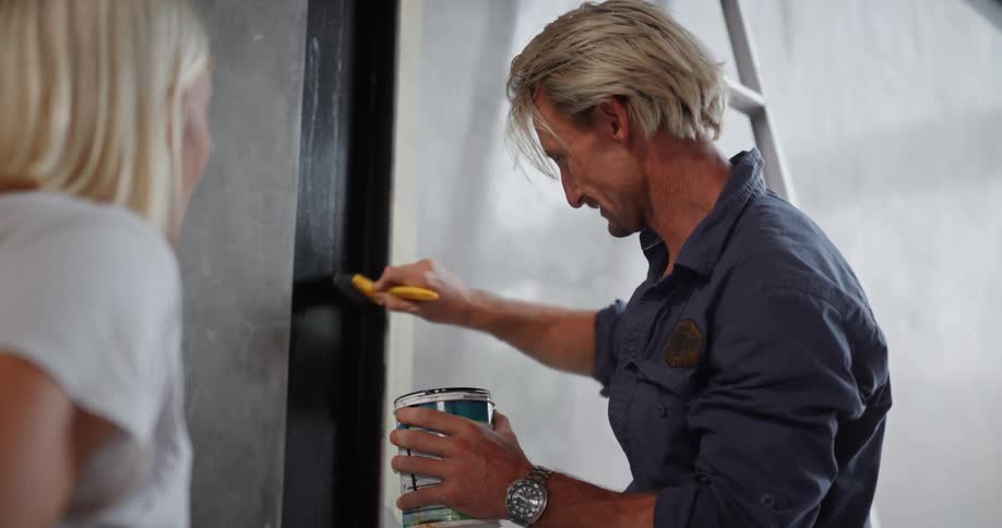 A man is holding a paint can and conversing with a woman while preparing to paint a wall