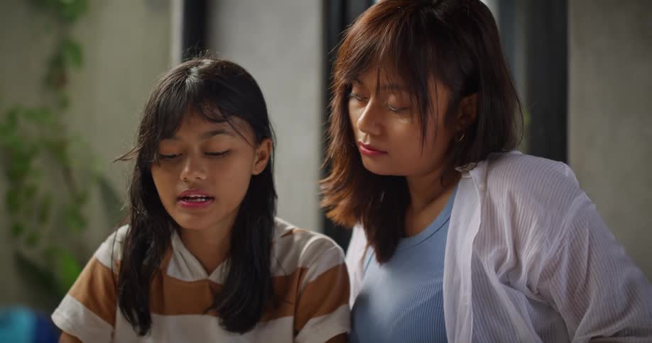 A young woman studies from a book speaking while an older woman looks on and occasionally gestures