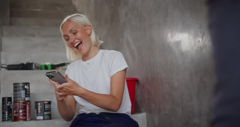 A woman sitting on a staircase talking and laughing with someone then using her smartphone