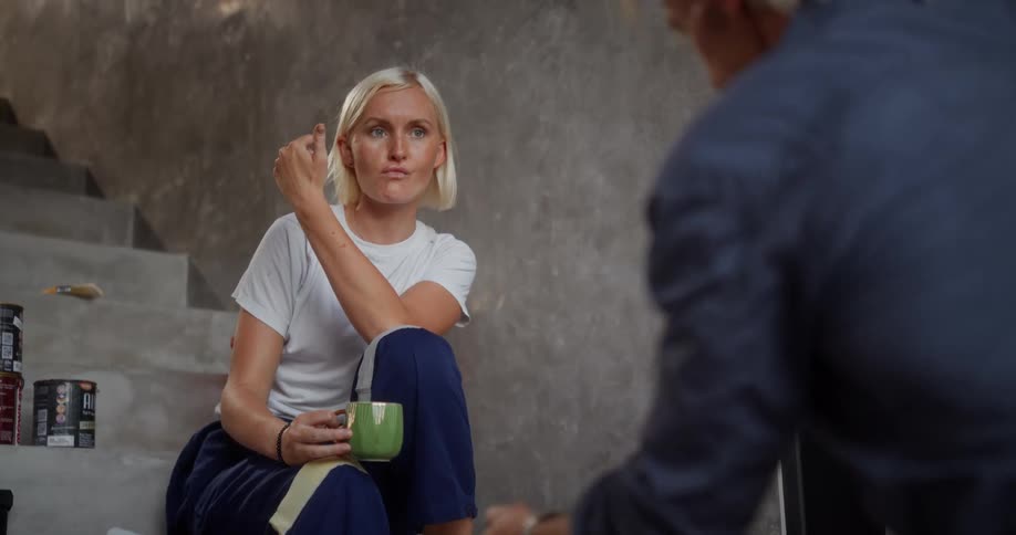 A woman sitting on a staircase with a cup in her hand talking to a man who is taking a ribbon from her