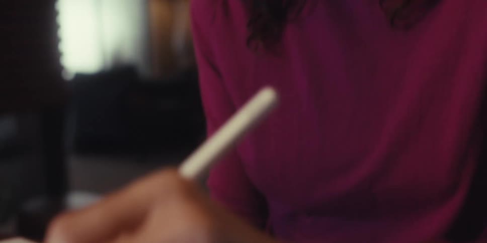 A focused woman writes on a tablet with a digital pen suggesting creativity and concentration
