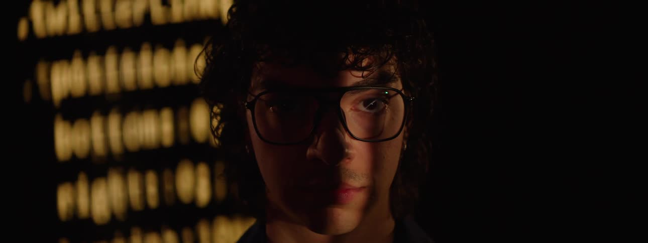 Portrait of a man wearing glasses and in the background a screen displaying numbers