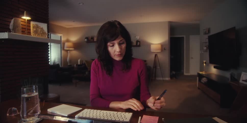 A woman is working at a desk and talking to someone on a video call in a modern warmly lit living room
