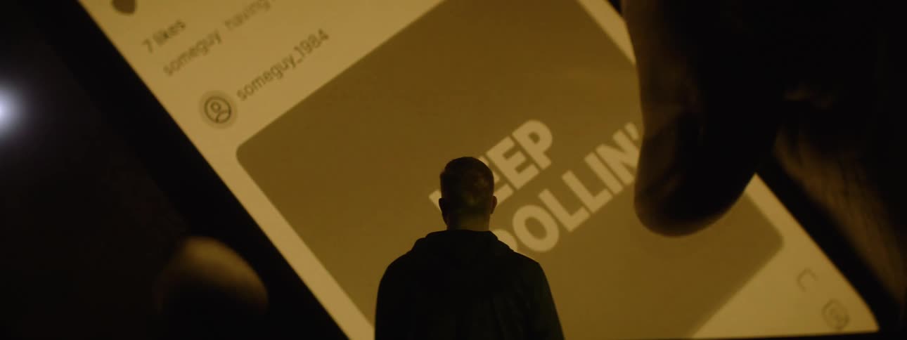 A man watches a projection on the wall of someone using their cell phone