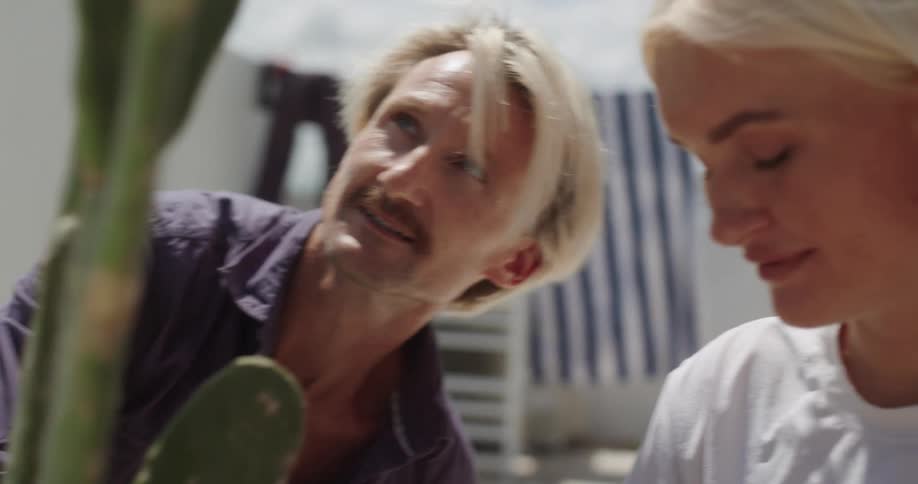A man and woman are gardening together outdoors in a bright sunny setting sharing a moment of affection