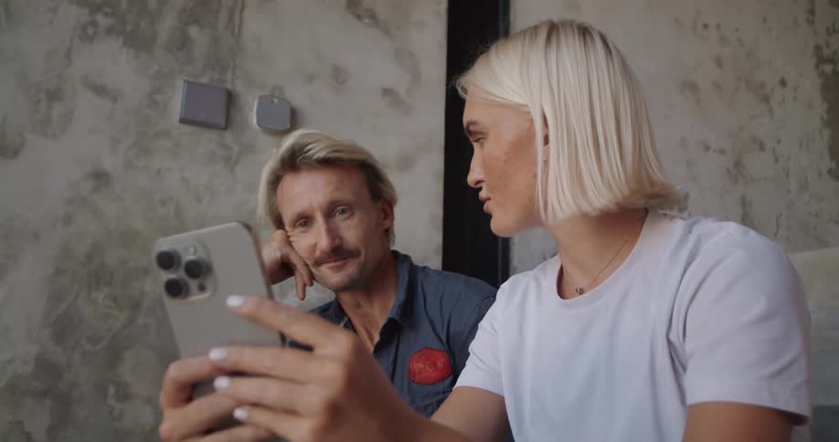 A man and a woman are using a cell phone and then they are talking and start laughing
