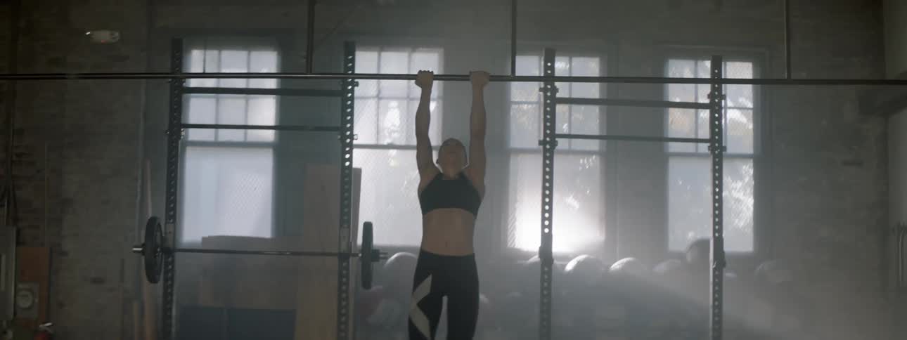 A woman jumps and pulls up on a pull up bar