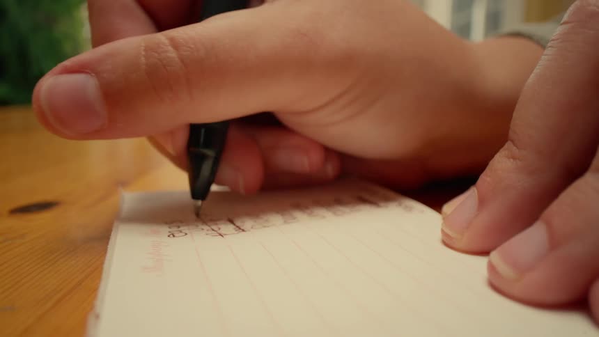 Hand with a pen writing on a small notepad