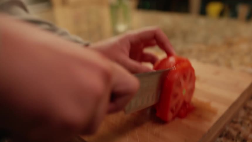 Hands with a knife cutting tomato slices