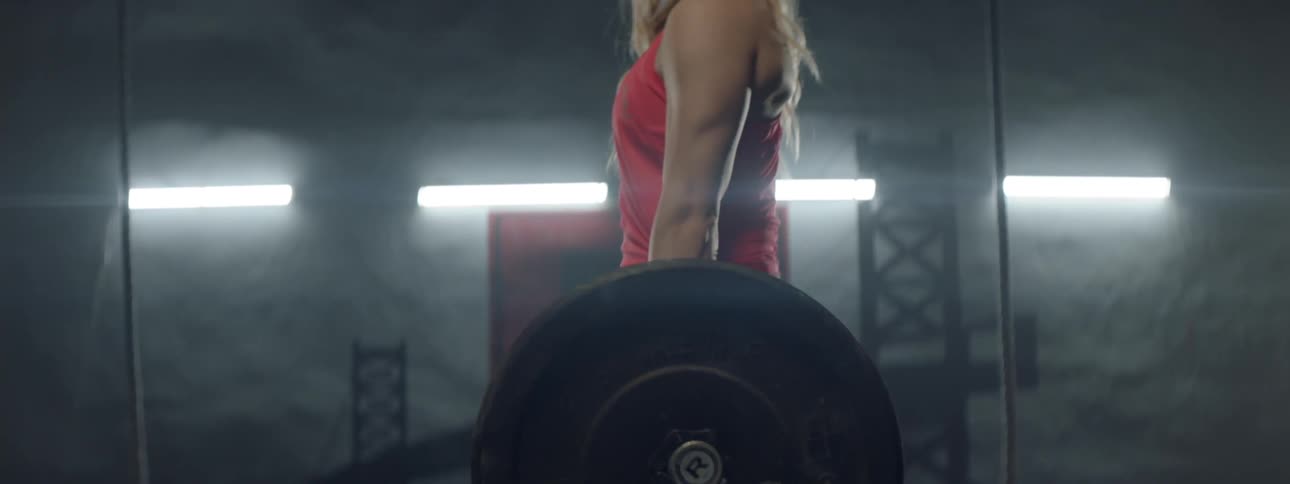 A woman bends and lifts a barbell with weights