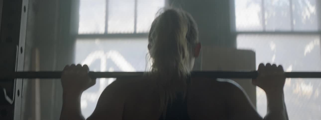 A woman climbs under a barbell and balances it on her shoulders