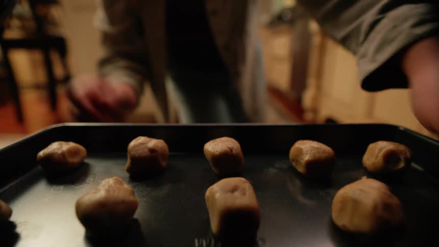 A person places a baking sheet filled with cookie dough balls into an oven