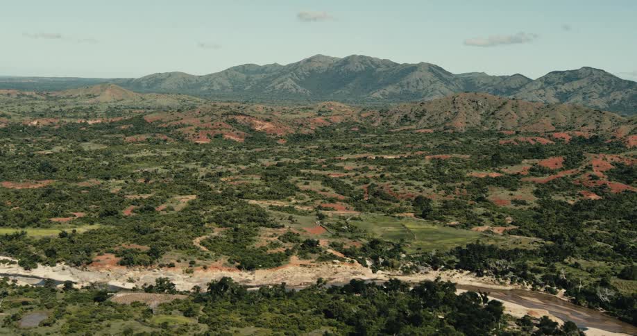 Groves of trees dot the hills and fields surrounding a river under a slightly cloudy sky