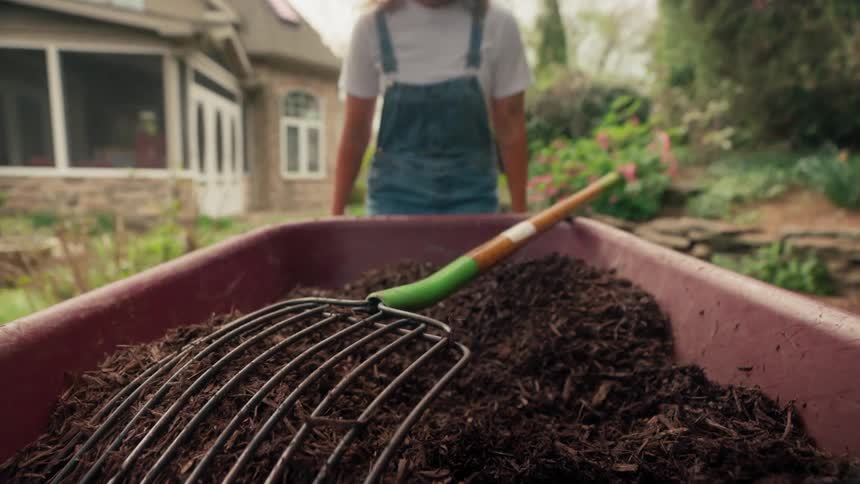 Woman in a backyard carrying a wheelbarrow with fertilizer