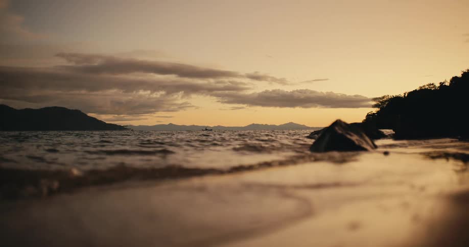Ocean waves move towards the sandy coast as the sun is setting